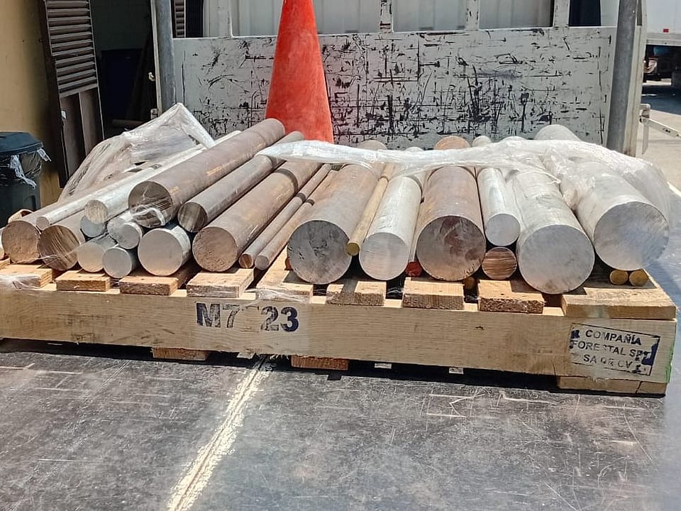 Barras redondas de acero, bronce, aluminio e inoxidable sobre tarima, listas para maquinado en torno